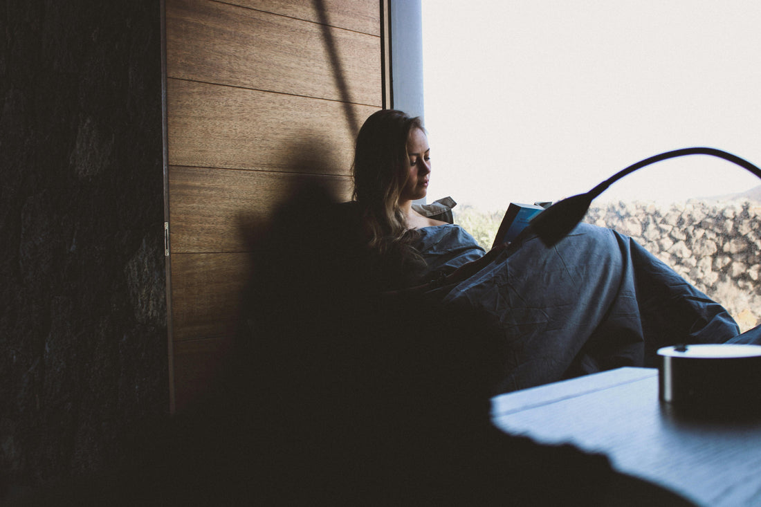 Peaceful moment of a woman sitting by a sunlit window reading a book, surrounded by soft natural light and a cozy home atmosphere – perfect inspiration for slow living and mindful relaxation.
