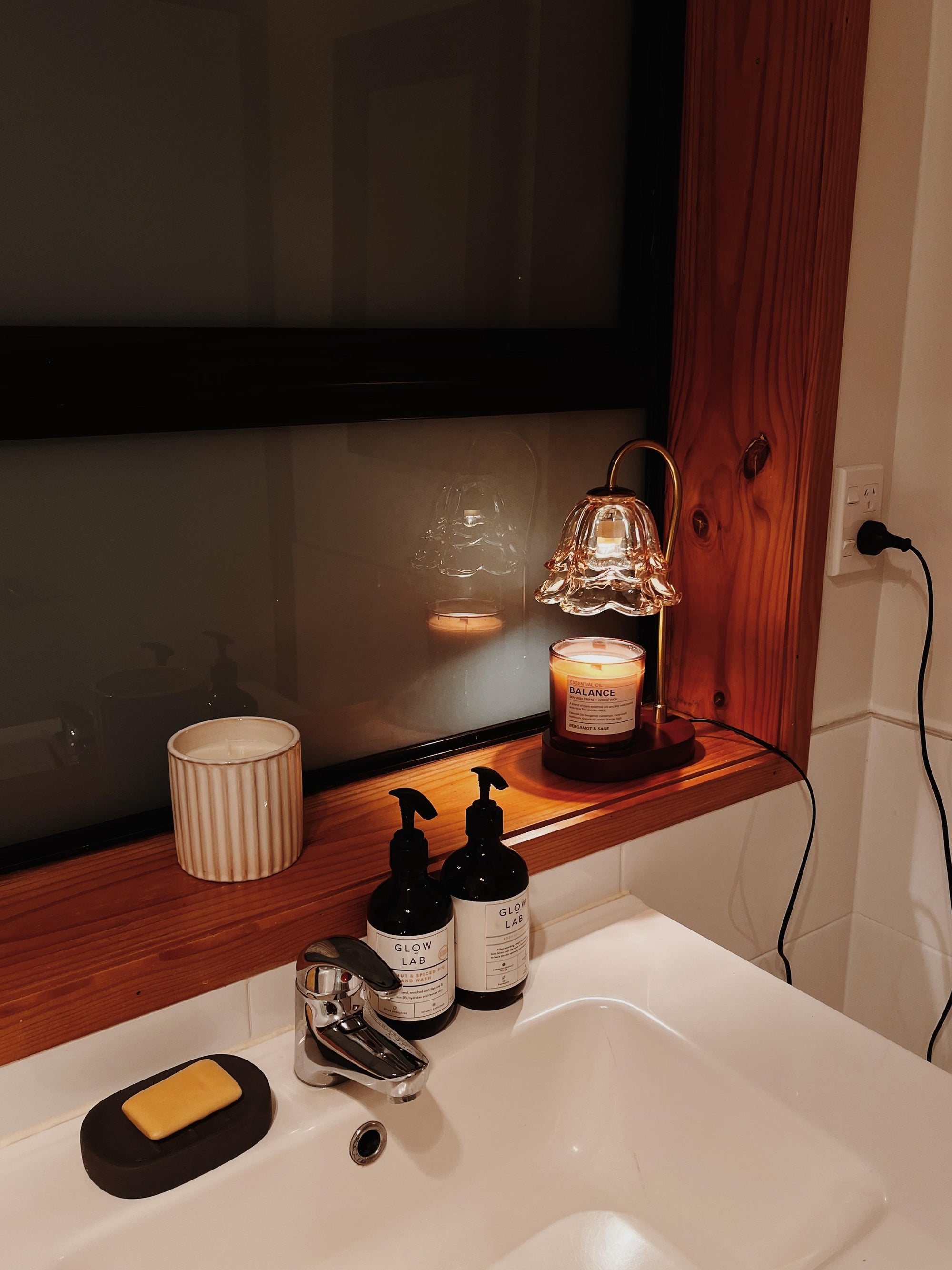 Auren Bloom Candle warmer lamp with a flower-shaped glass shade melting a Balance-scented candle on a bathroom windowsill, creating a cozy and serene ambiance