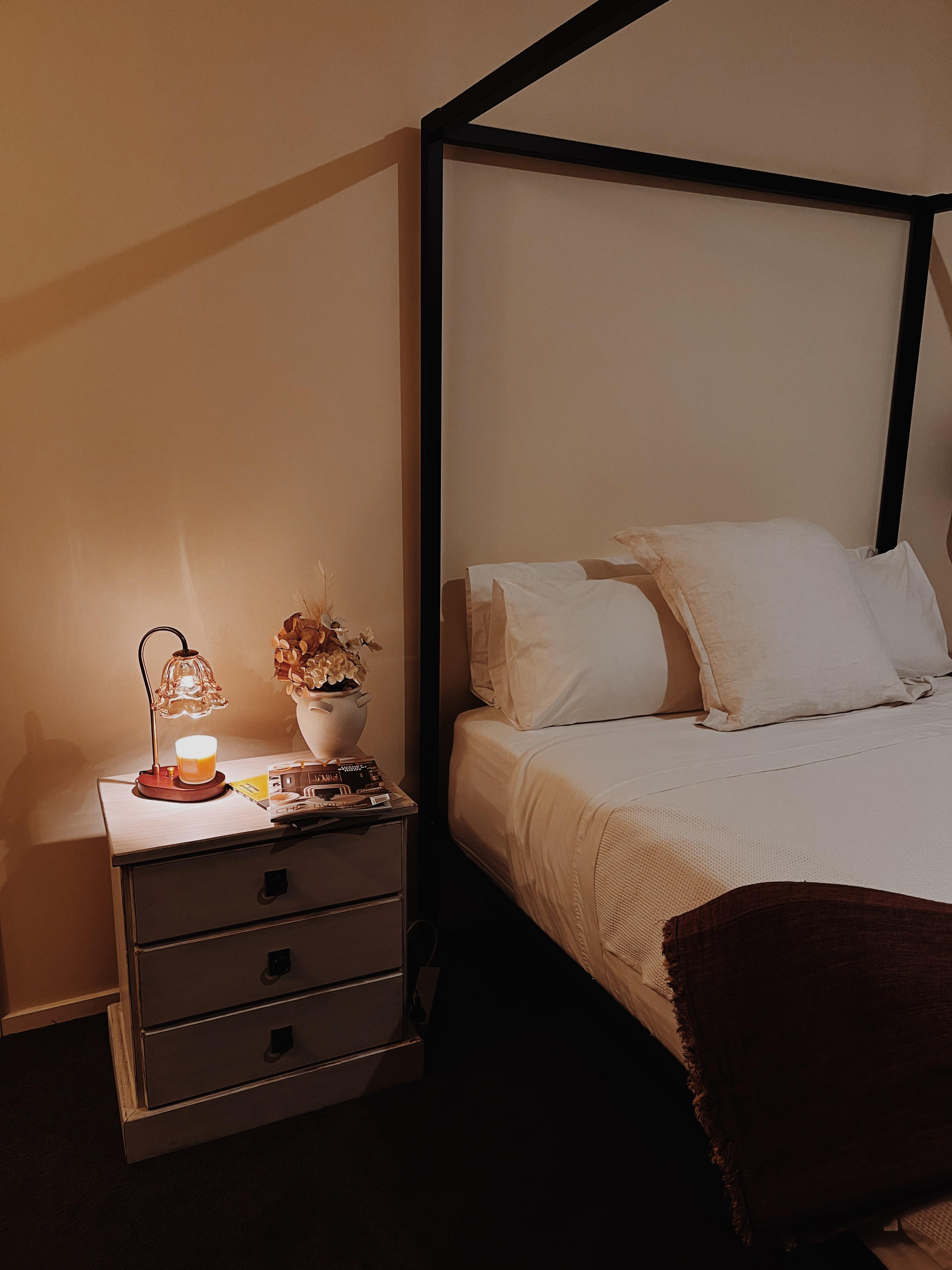 Auren Bloom Candle Warmer shown in a Warm and cozy bedroom scene featuring the vintage-style candle warmer on a nightstand with dried flowers and home decor magazines.