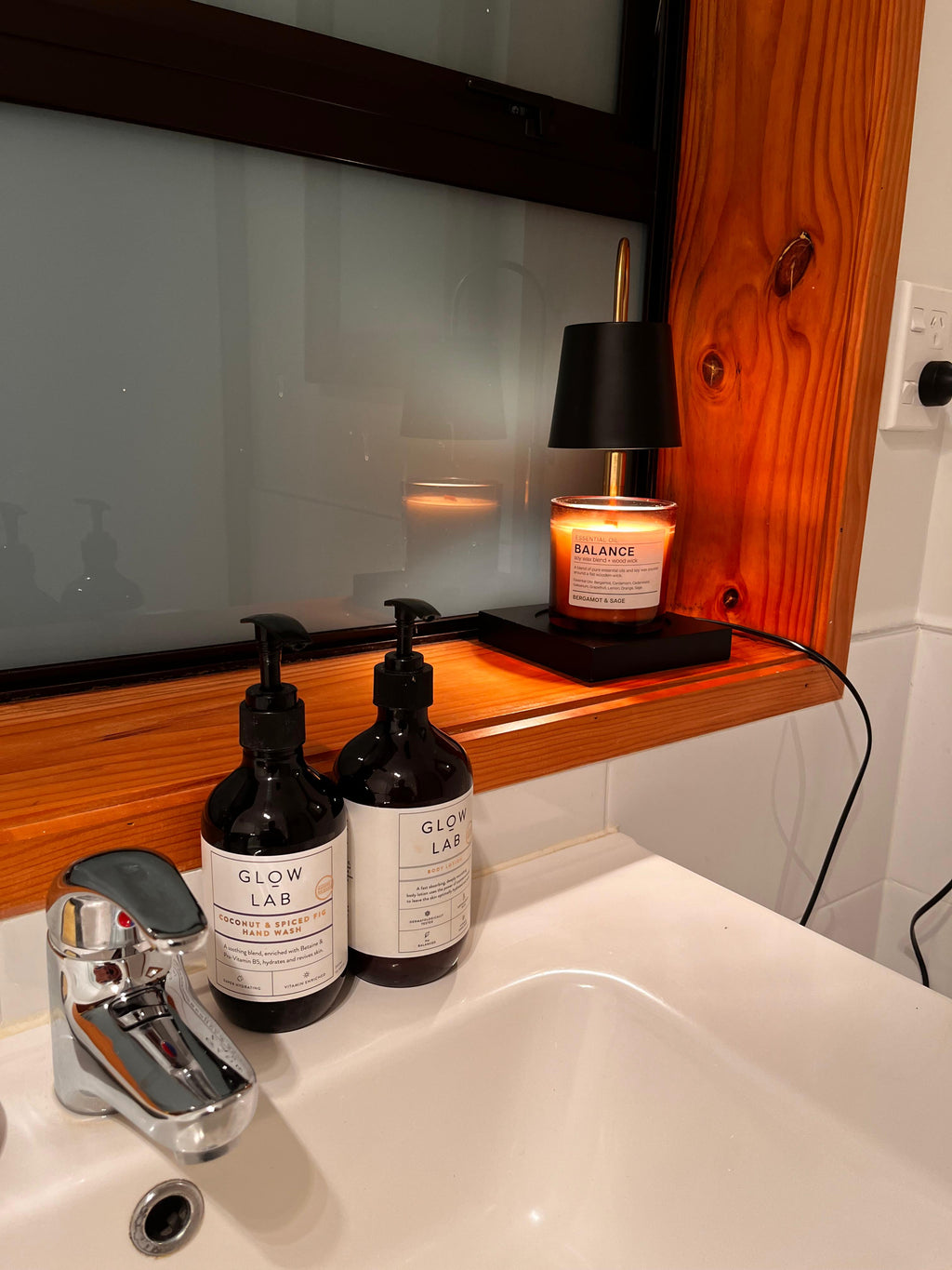 Auren Modern Candle Warmer close-up view on a bathroom windowsill, softly melting a creamy candle and casting a gentle light over nearby sink essentials—capturing the cozy, calming essence of a nighttime self-care ritual.