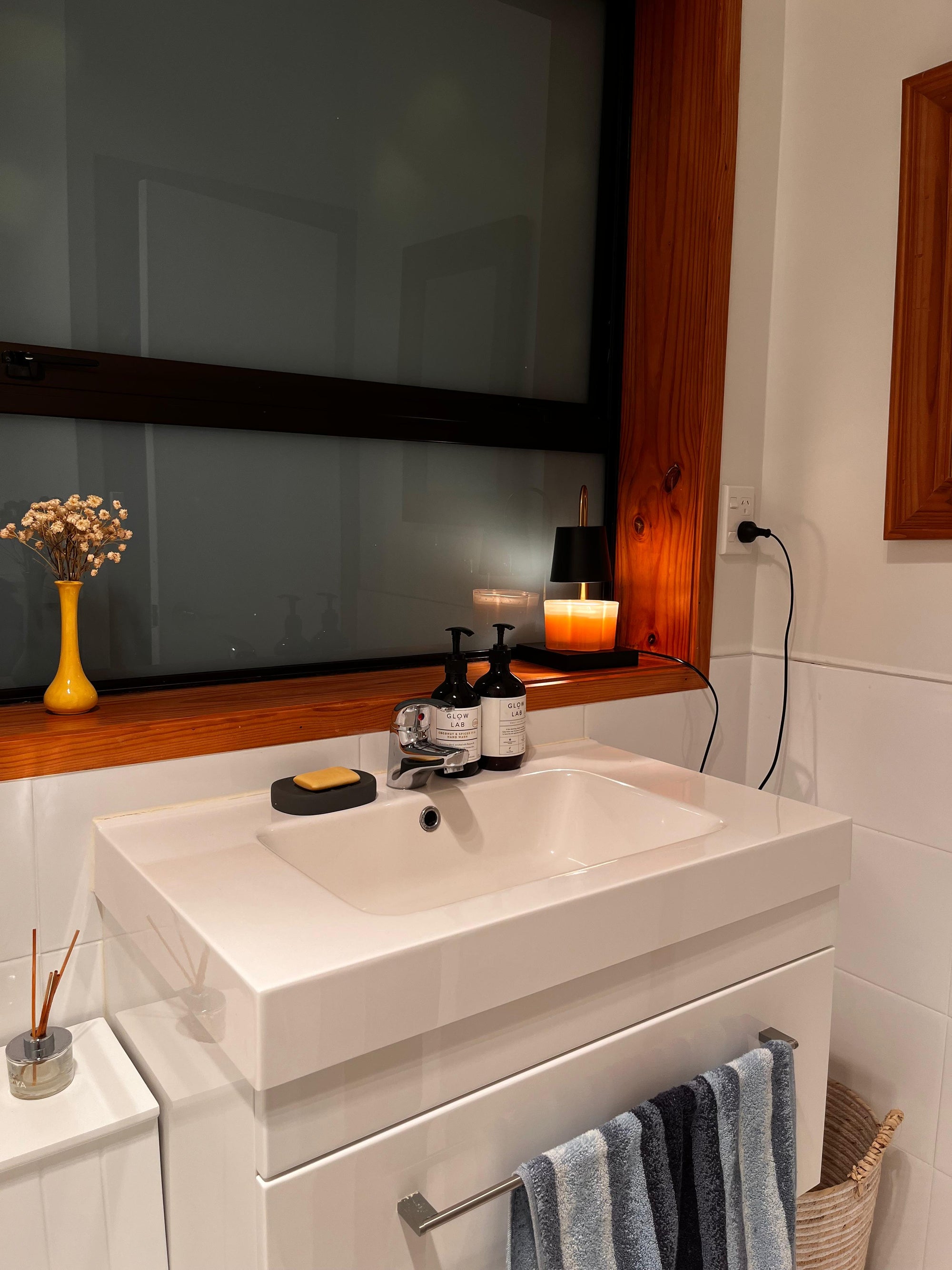 Auren Modern Candle Warmer gently melts a scented candle beside a modern bathroom sink, surrounded by soft towels, natural wood tones, and minimal decor—creating a serene aromatherapy experience for peaceful, end-of-day unwinding.