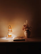 Auren Elegance Candle Warmer softly illuminating a cozy wooden tabletop with an autumnal dried flower arrangement and a design magazine, creating a serene home ambiance.