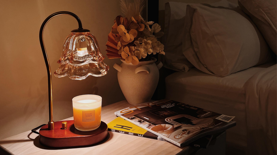 Cozy bedroom nightstand with a glowing candle warmer, soft lighting, and styled decor